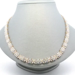 Floral Cluster Diamond Necklace. A continuous motif of diamond-studded floral clusters defines this intricate necklace. Crafted in yellow gold, the design links multiple diamond arrangements to create a seamless collar silhouette. The articulated links allow the piece to drape comfortably along the neckline